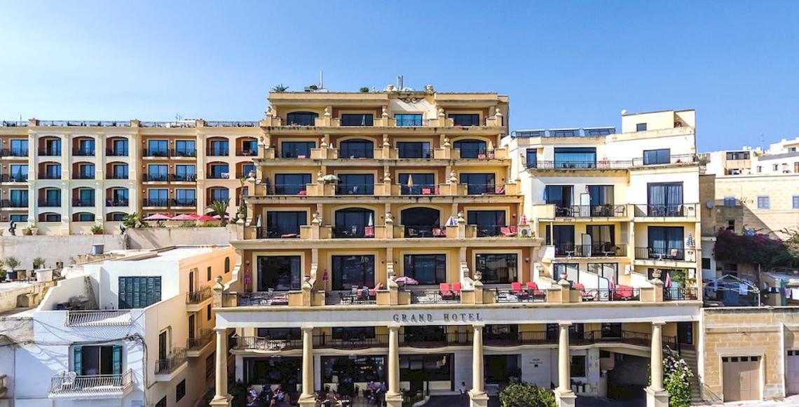Außenansicht des Grand Hotel Gozo mit mehreren Stockwerken, Balkonen und Gästebereichen.