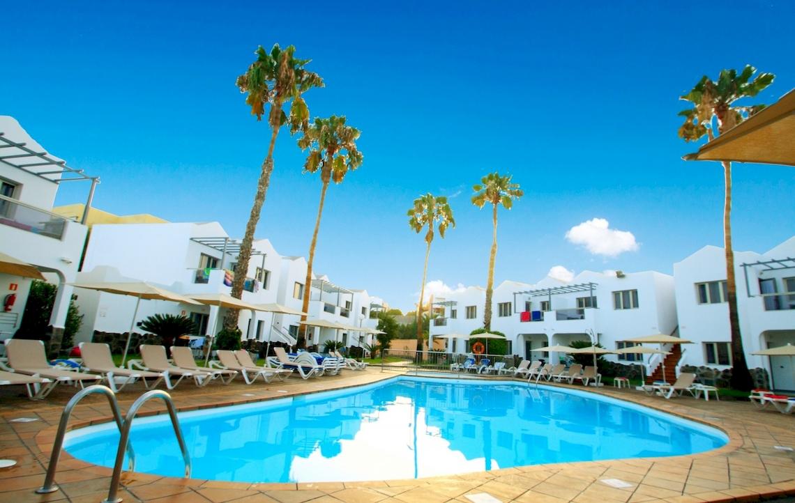 Poolbereich im Turbo Club mit weißen Gebäuden und Sonnenliegen unter Palmen.