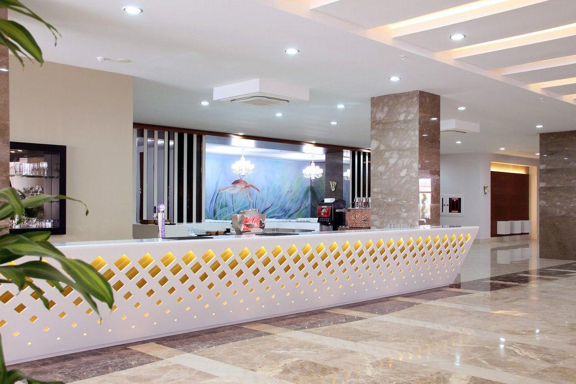 Rezeption im Adalya Ocean Deluxe Hotel mit weißer Theke und goldenen Diamantmustern.