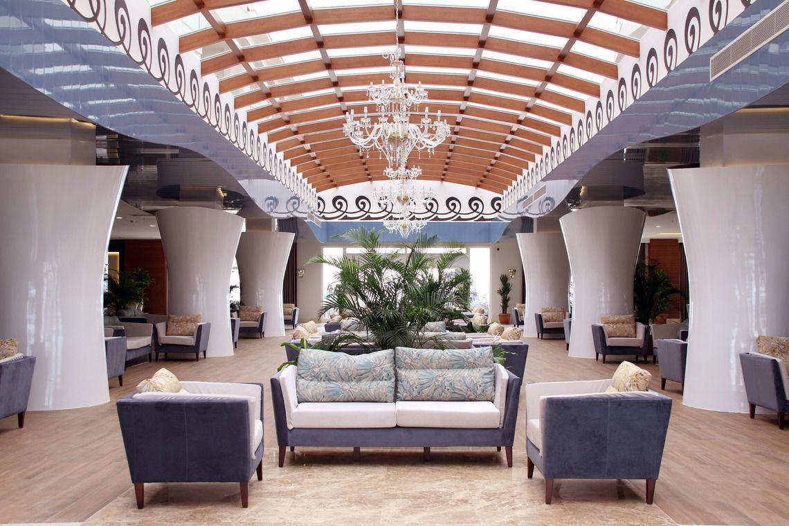 Innenansicht der Lobby des Adalya Ocean Deluxe Hotels mit weißen Säulen und einem Kristall-Chandelier.