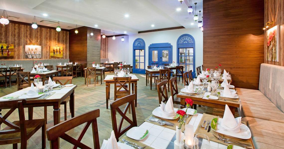 Innenansicht des Restaurants des Adalya Ocean Deluxe Hotels mit gedeckten Tischen und dekorierten Wänden.