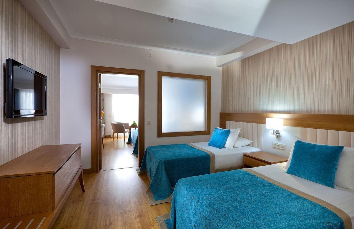Innenansicht eines Doppelzimmers im Adalya Ocean Deluxe Hotel mit zwei Betten, Nachttischen, Fernseher und Spiegeltür.