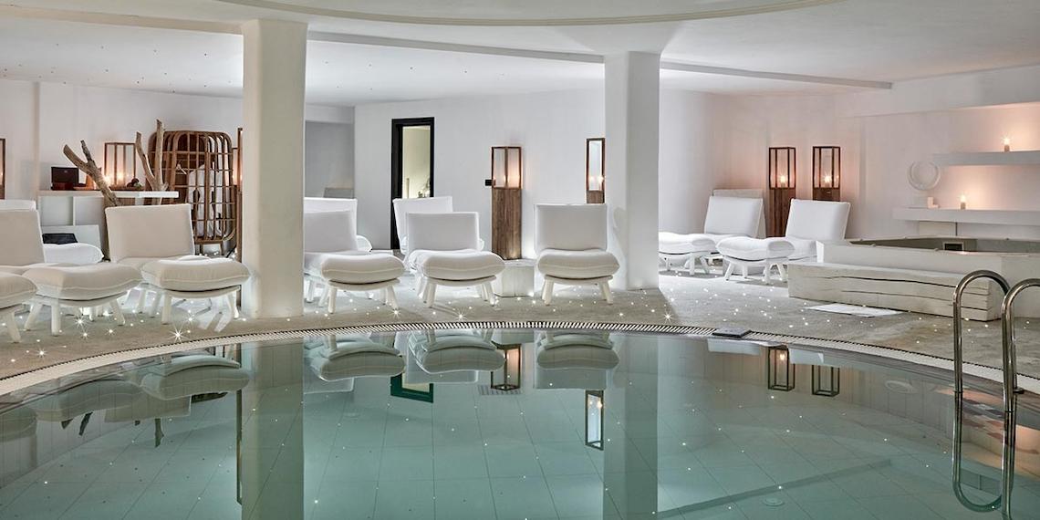 Innenbereich des Royal Myconian Resorts mit Pool, weißen Möbeln und weichen Kissen.