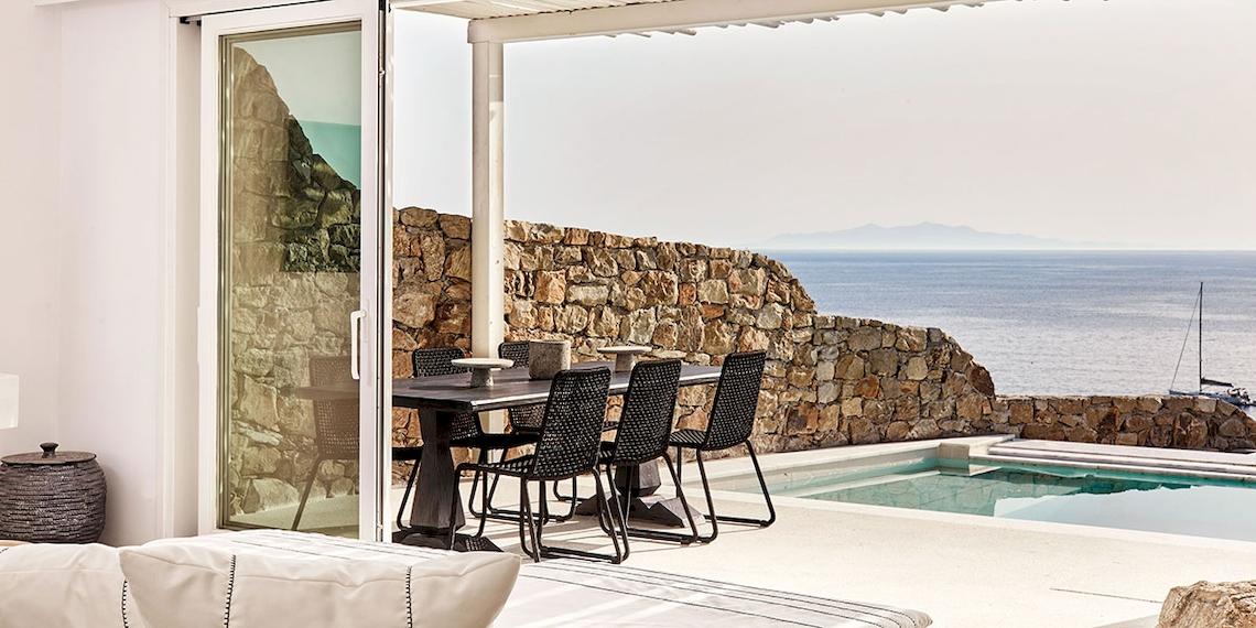 Terrasse des Royal Myconian Resorts mit Blick auf das Meer und eine Steinmauer.