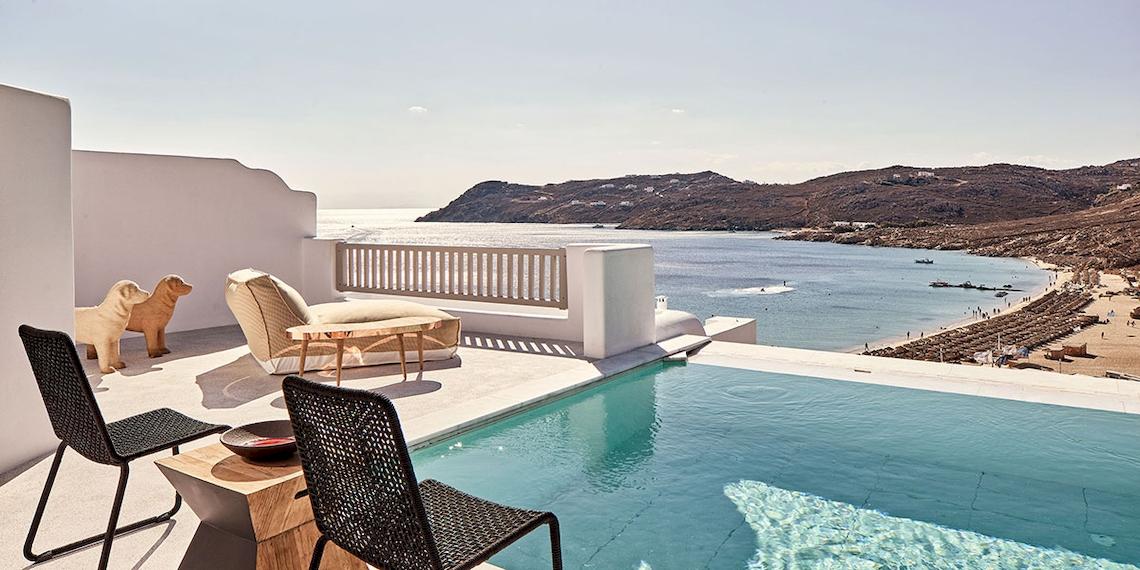 Royal Myconian Resort Balkon mit Pool und Meerblick, Hundestatue und Loungesofa.