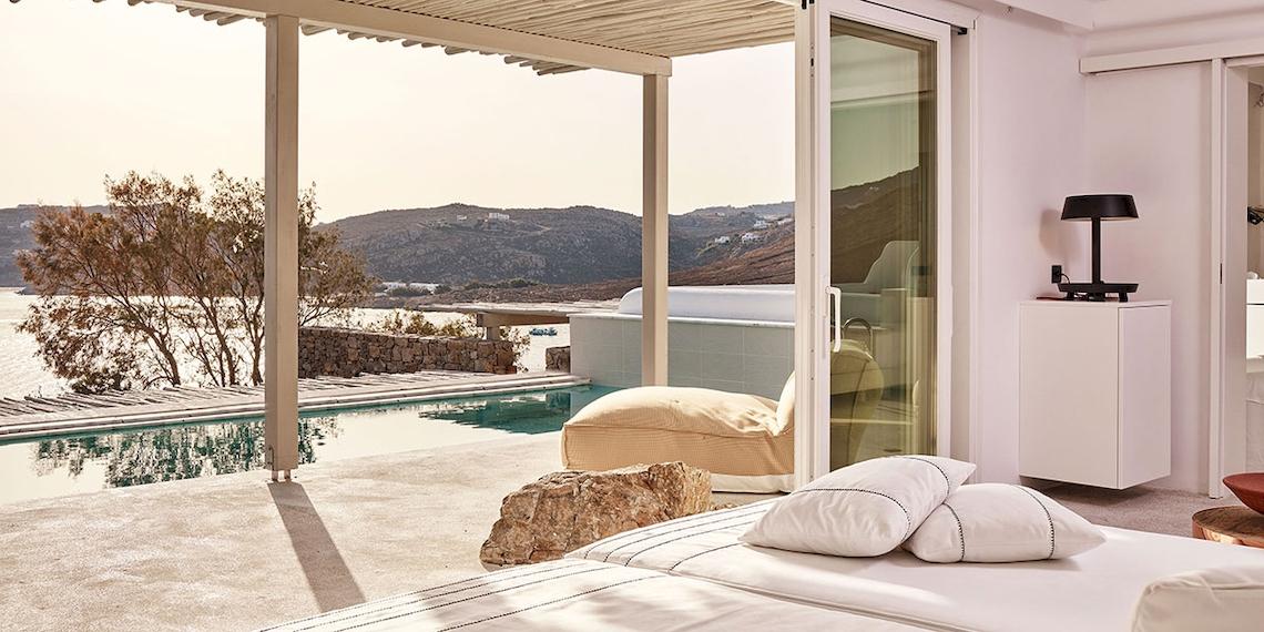 Terrasse des Royal Myconian Resorts mit Pool und Meerblick, Möbel und Lampe sind zu sehen.
