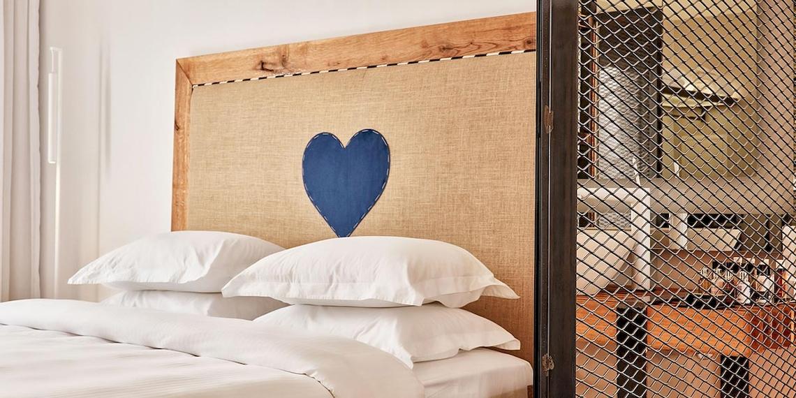 Bett im Royal Myconian Resort mit blauem Herz auf dem Kopfteil