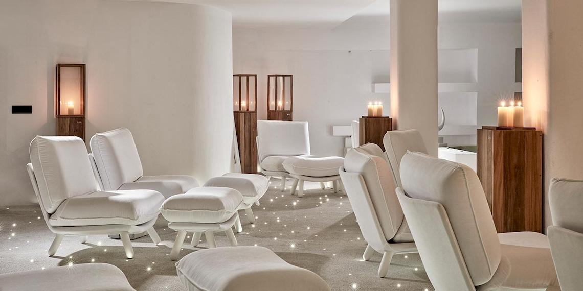 Weißer Loungebereich im Royal Myconian Resort mit weißen Sesseln, runden Hockern und brennenden Kerzen.