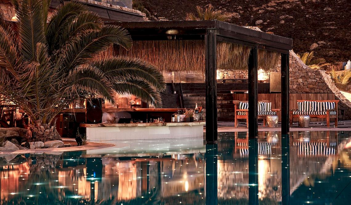 Poolbar des Royal Myconian Resorts mit Palme und beleuchtetem Pool.