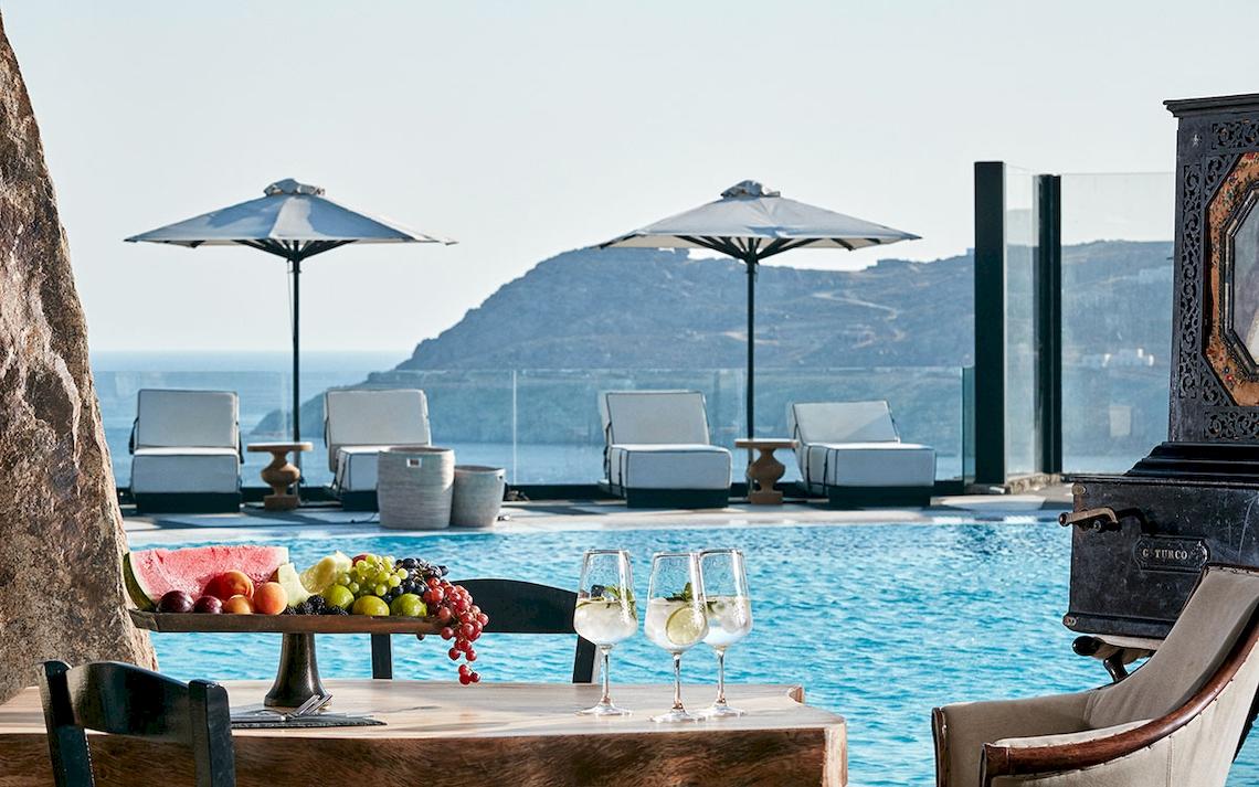 Poolbereich des Royal Myconian Resorts mit Blick aufs Meer und Obstkorb auf dem Tisch