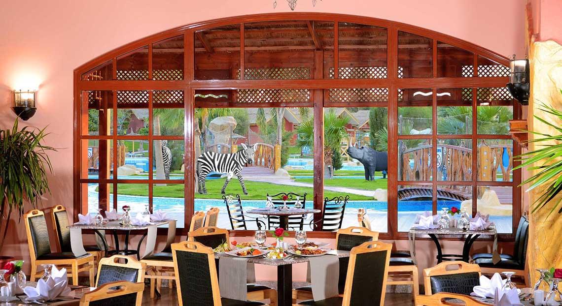 Innenansicht des Restaurants im Pickalbatros Jungle Aqua Park Resort mit Blick auf einen Swimmingpool und Tiere.