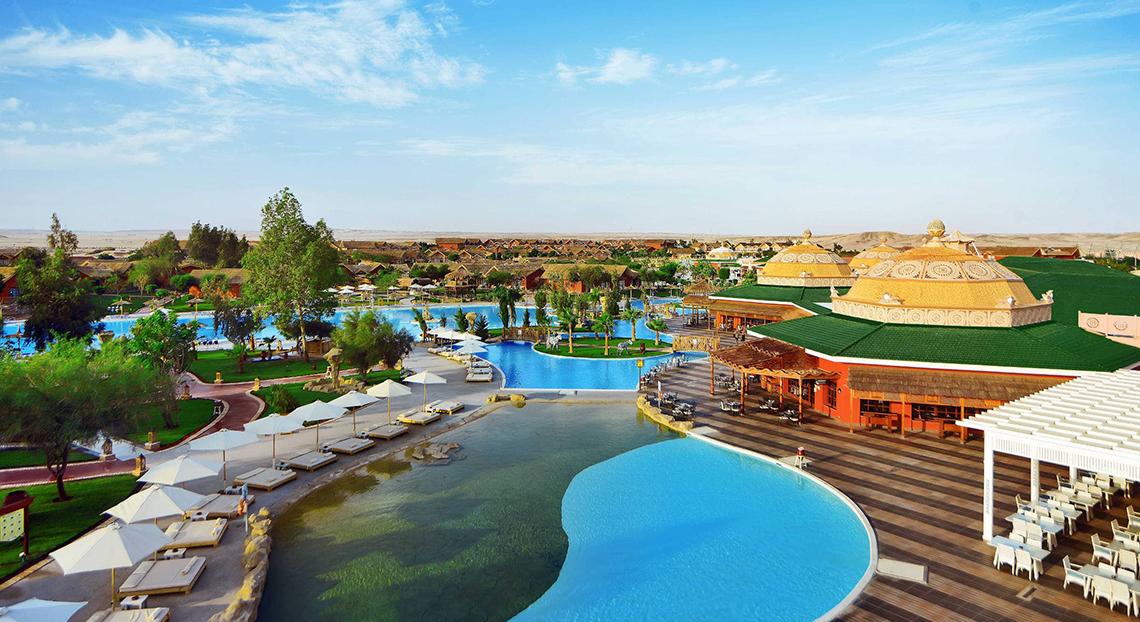 Außenansicht des Pickalbatros Jungle Aqua Park Resorts mit Swimmingpools, Sonnenliegen und grünem Dach.
