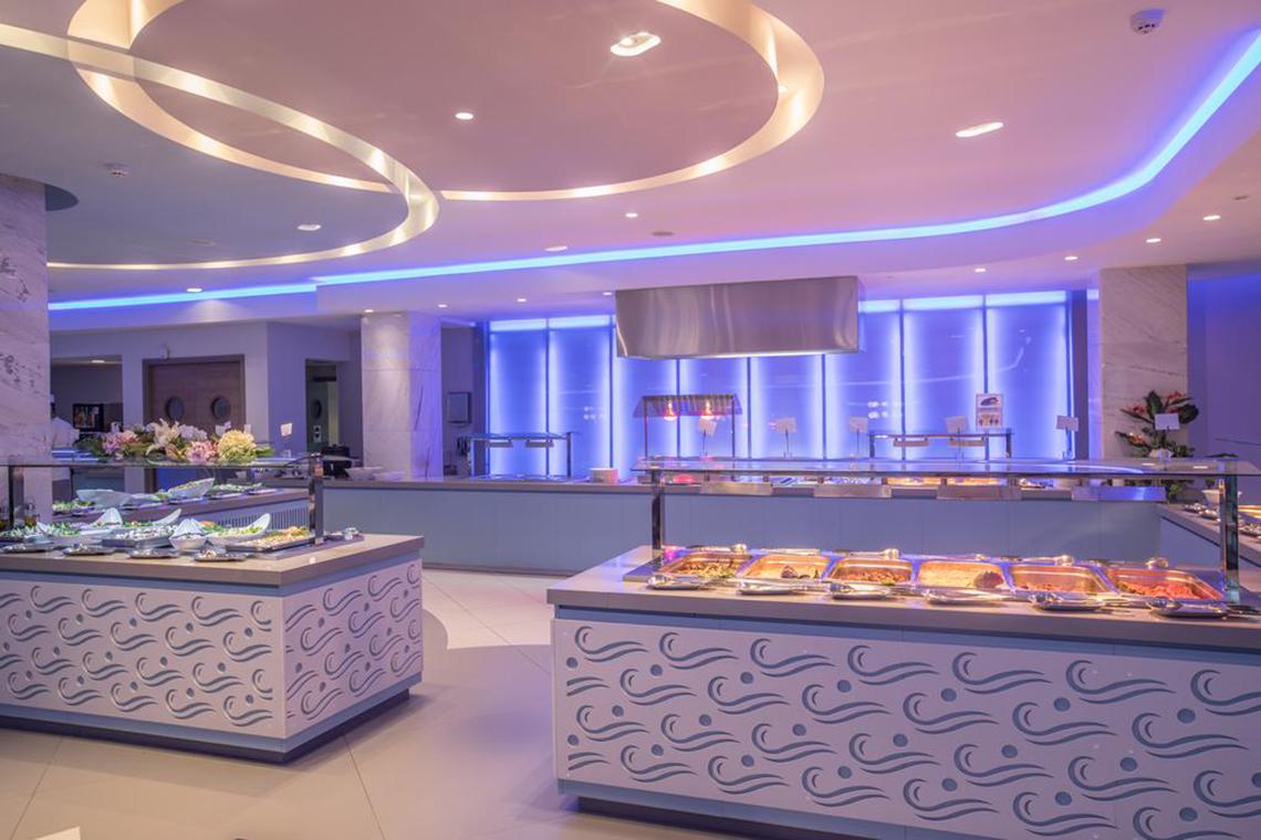 Innenbereich des Vassos Nissi Plage Restaurants mit geometrischen Mustern, blauen Lichtern und Büfetttischen.