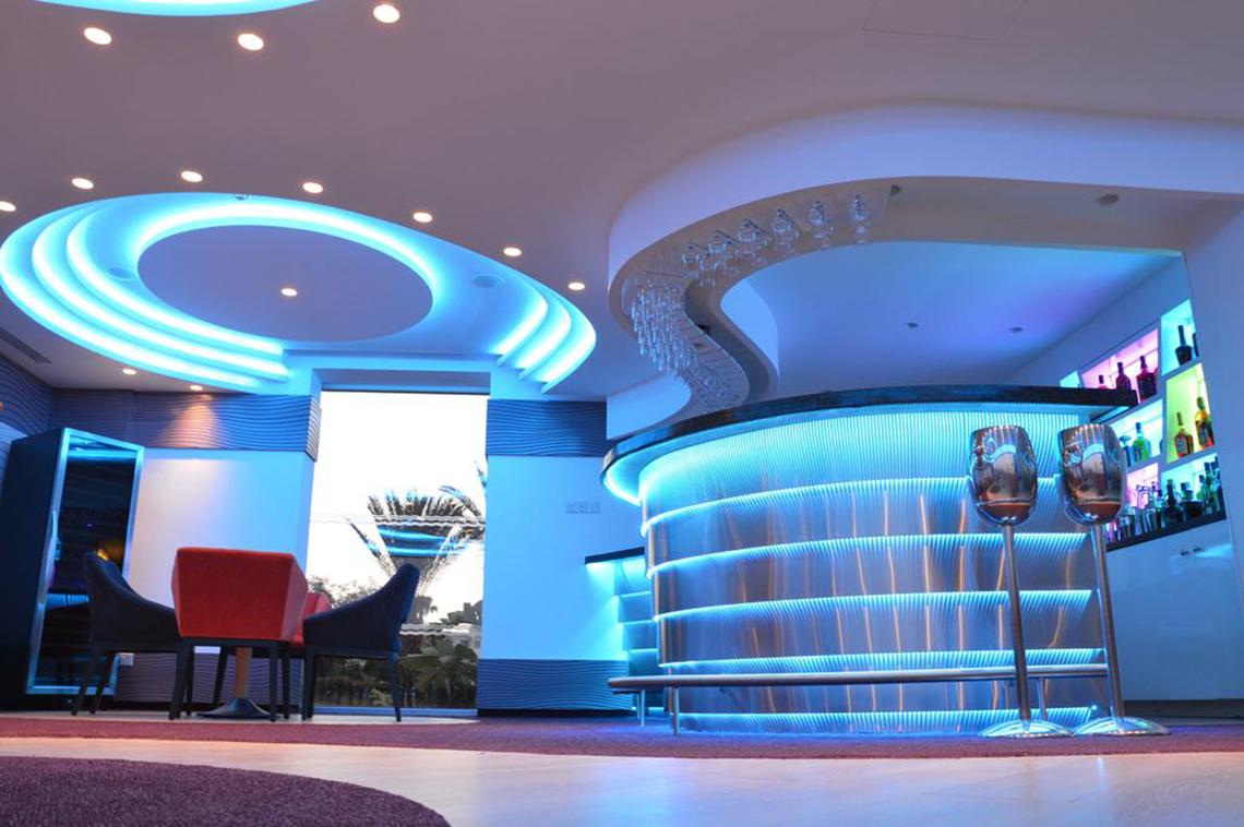 Innenansicht der Bar im Vassos Nissi Plage Hotel mit blauen Beleuchtungselementen und modernen Möbeln.