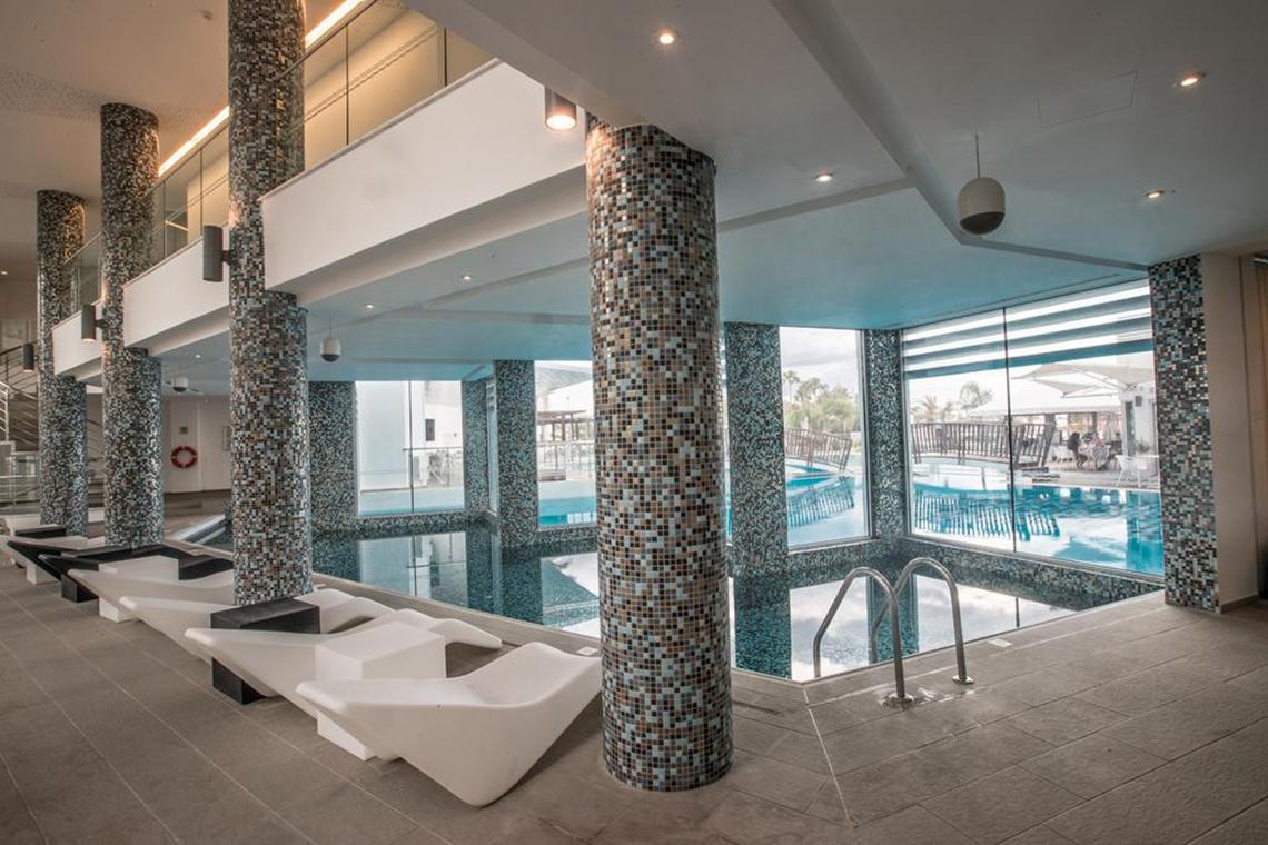 Pool-Loungebereich im Vassos Nissi Plage Hotel mit weißen Liegestühlen und gefliesten Säulen.