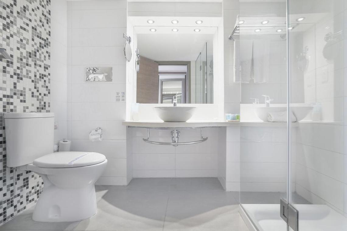 Modernes Badezimmer im Vassos Nissi Plage Hotel mit weißem Design und Glasdusche.