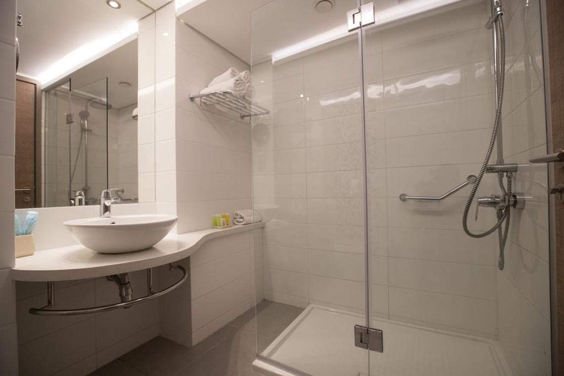 Ein modernes Badezimmer im Vassos Nissi Plage Hotel mit einer Dusche, Waschbecken und Handtüchern.