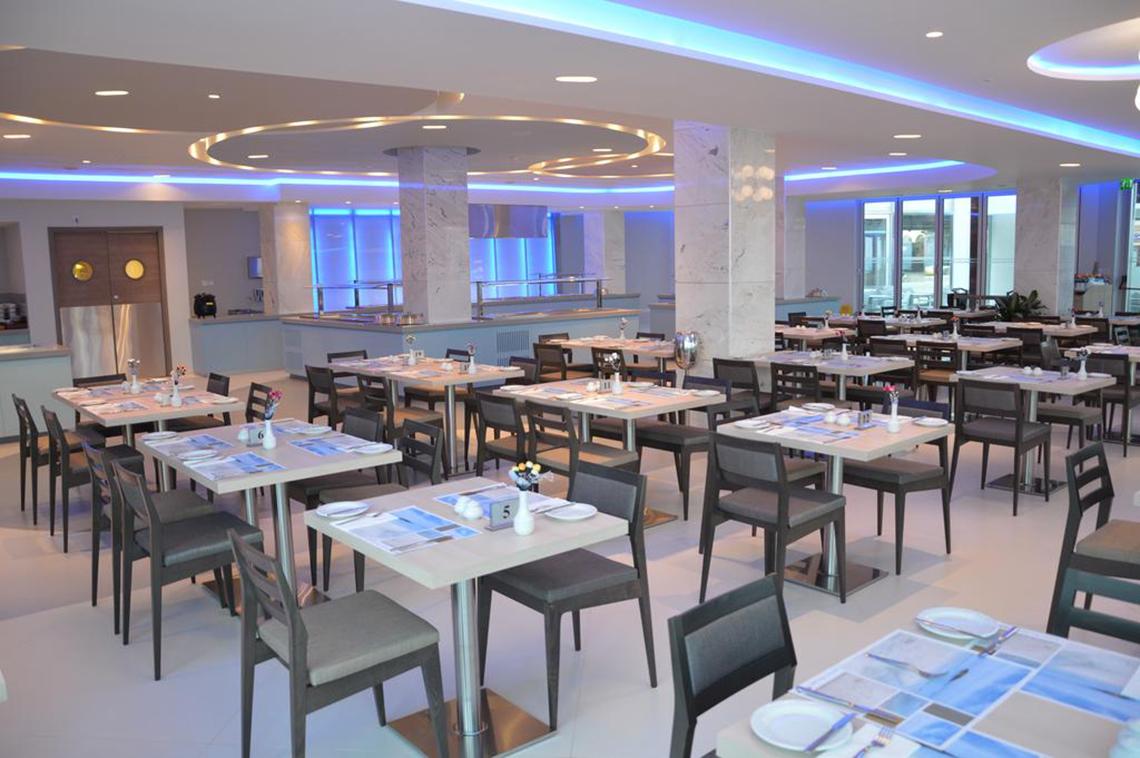 Innenansicht des Restaurants im Vassos Nissi Plage Hotel mit modernen Möbeln und blauen Beleuchtungselementen.
