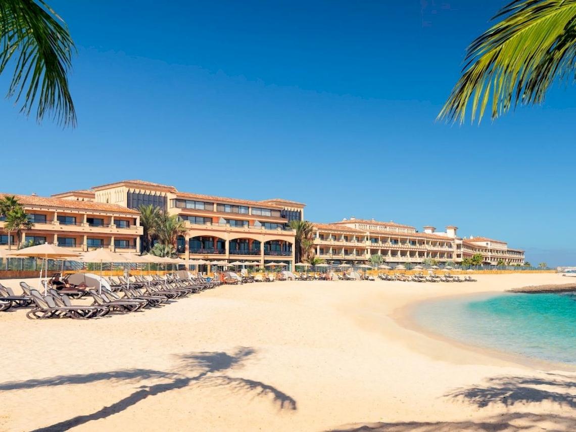Strand des Secrets Bahia Real Resort & Spa mit vielen Liegestühlen und einem großen Hotelgebäude