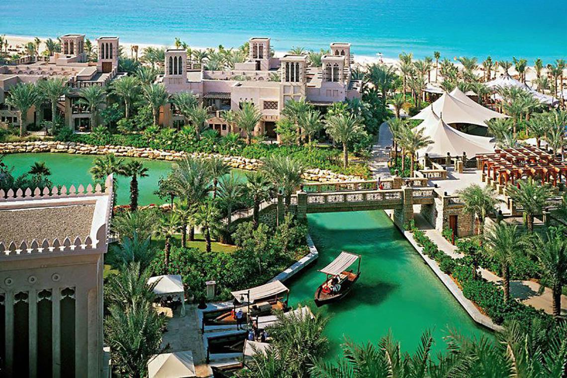Luftaufnahme des Jumeirah Dar Al Masyaf Resorts mit grünem Wasserkanal und traditioneller Architektur.