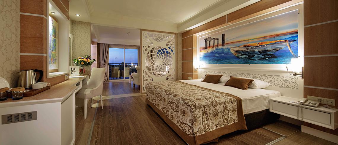 Innenansicht des Crystal Sunset Luxury Resort & Spa Hotelzimmers mit einem großen Bett, Nachttischen und einem Ausblick auf den Hafen.