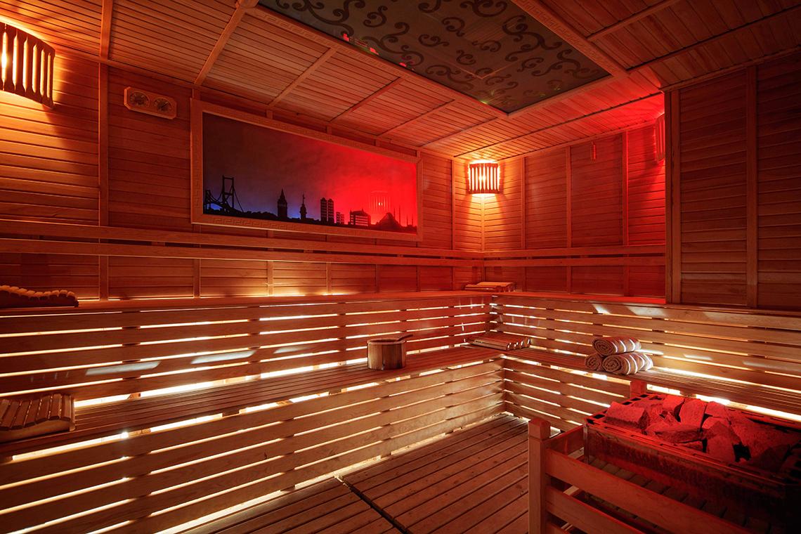 Innenansicht der Sauna im Crystal Sunset Luxury Resort & Spa mit Holzwänden und roter Beleuchtung.