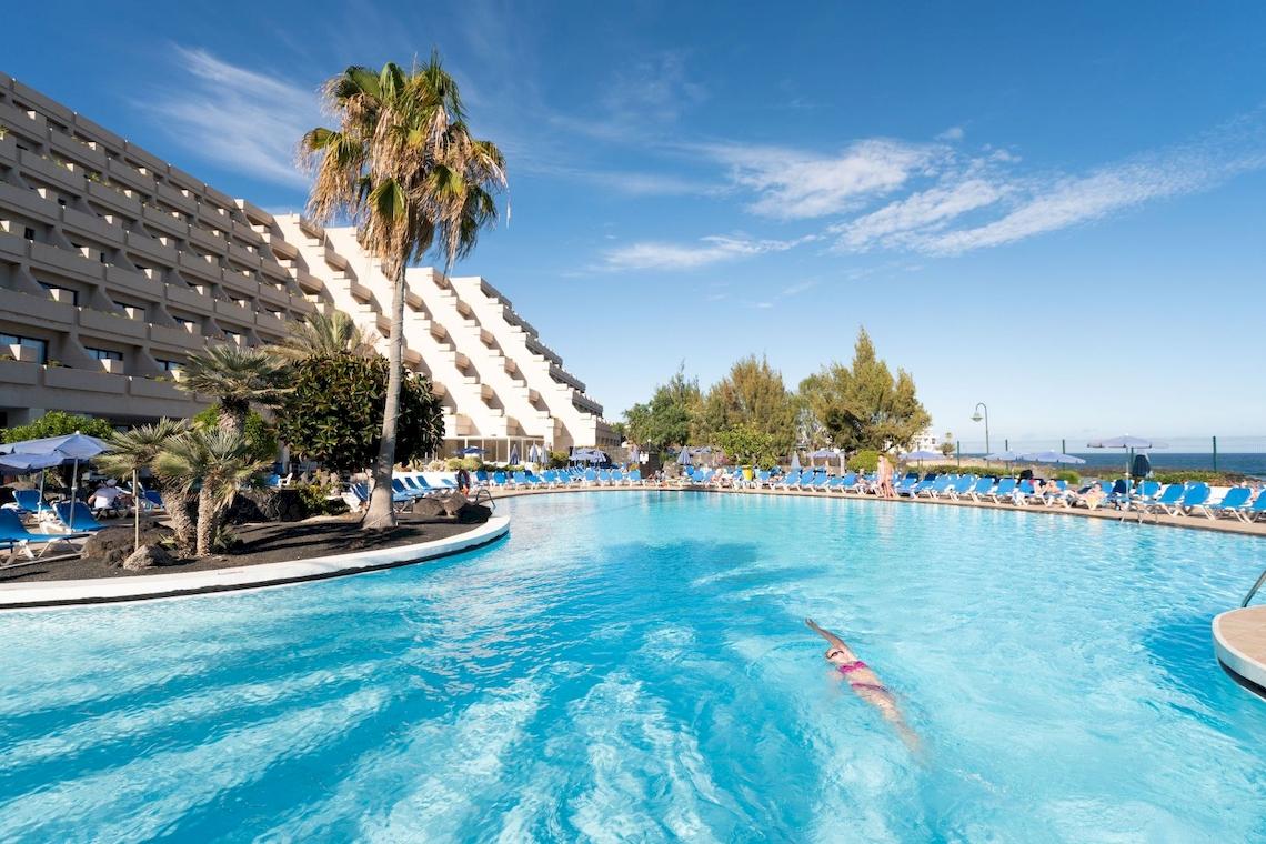 Ein Schwimmbad im Grand Teguise Playa Hotel mit Sonnenliegen und Palmen