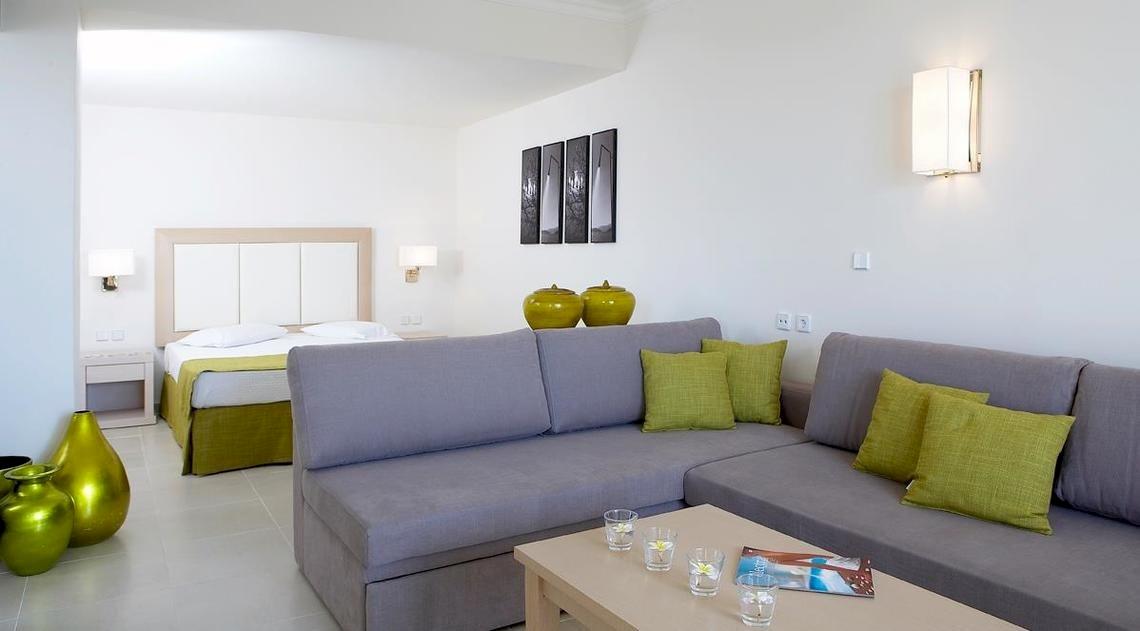 Innenansicht eines Zimmers im Electra Palace Rhodes Hotel mit Doppelbett, Sofa, grünen Vasen und modernen Lampen.