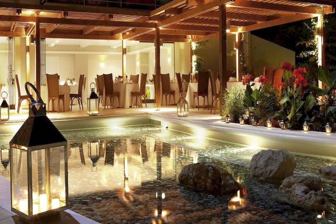 Außenbereich des Electra Palace Hotels bei Nacht mit beleuchteten Tischen und Stühlen.