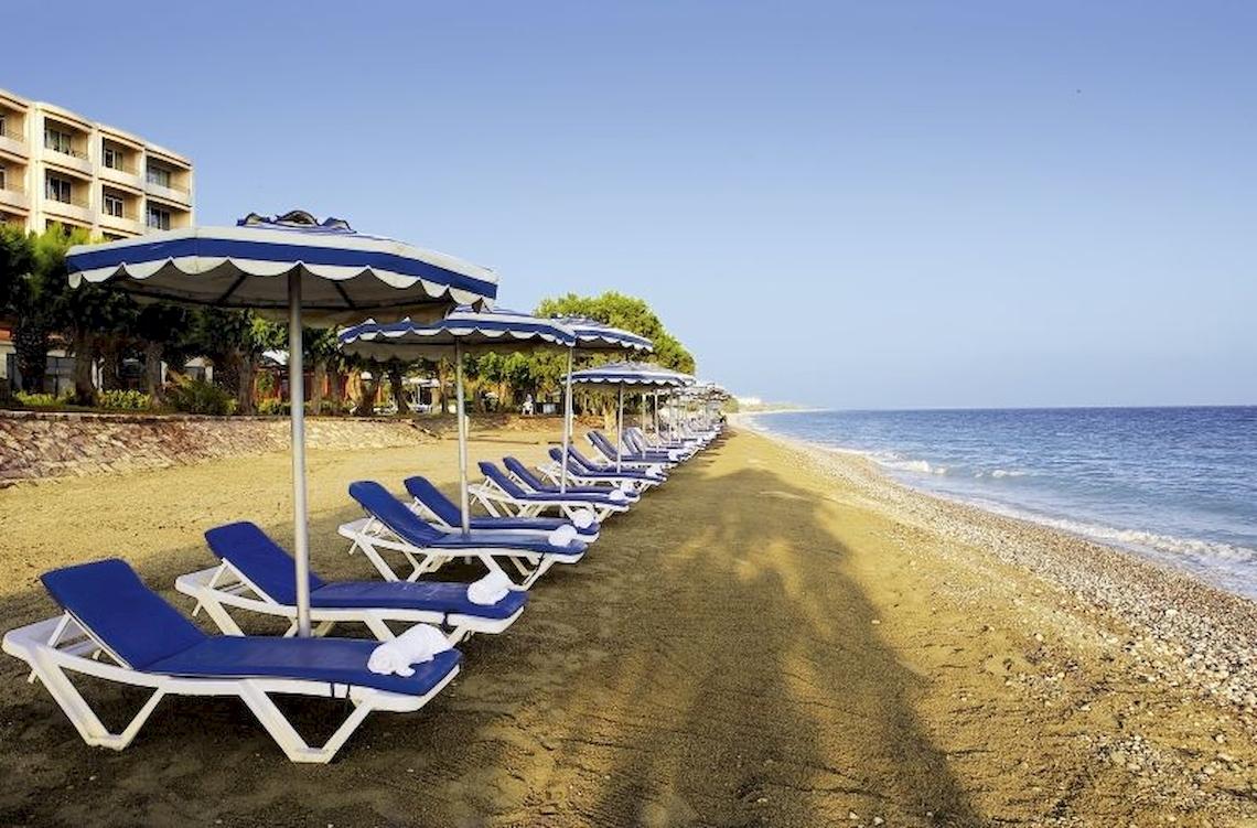 Reihe von Liegestühlen mit Sonnenschirmen auf dem Strand vor dem Electra Palace Rhodes Hotel