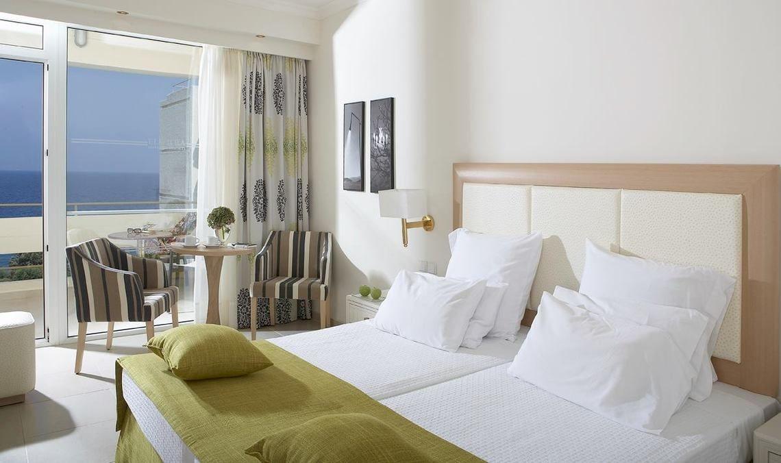Doppelzimmer im Electra Palace Rhodes mit Meerblick, inklusive Balkon, Tisch, Stühlen und Bett mit weißen Kissen.