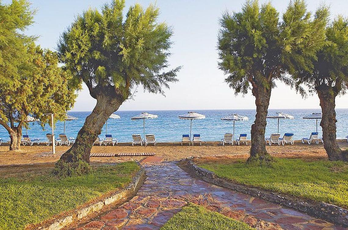 Strandbereich des Electra Palace Rhodes Hotels mit Bäumen, Sonnenliegen und Schirmen.
