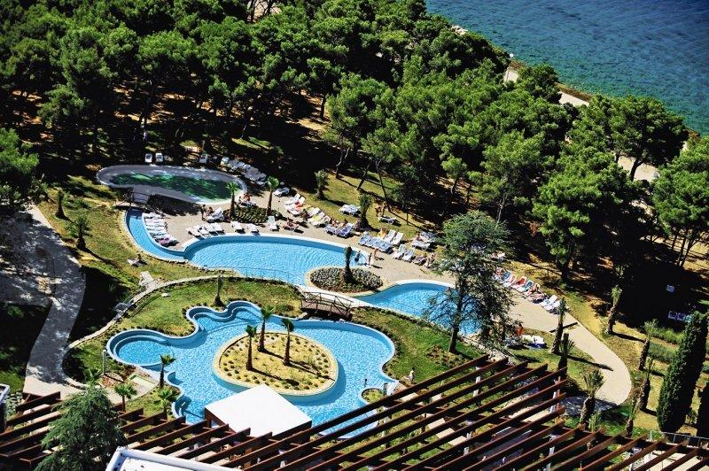 Aussenansicht des Schwimmbadbereichs des Niko Hotels mit mehreren Pools und Liegen.