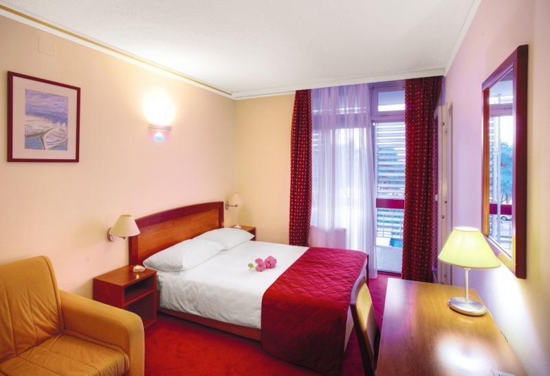 Innenansicht eines Hotelzimmers im Niko Hotel mit Bett, Lampe und Dekor.