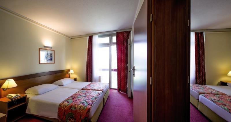 Innenansicht eines Doppelzimmers im Niko Hotel mit zwei Betten, Nachttischen und Lampen.