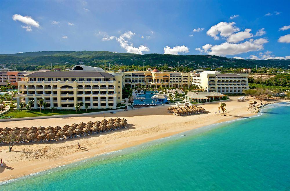 Luftaufnahme des Iberostar Grand Rose Hall Hotels mit Pool, Strand und Bergen im Hintergrund.