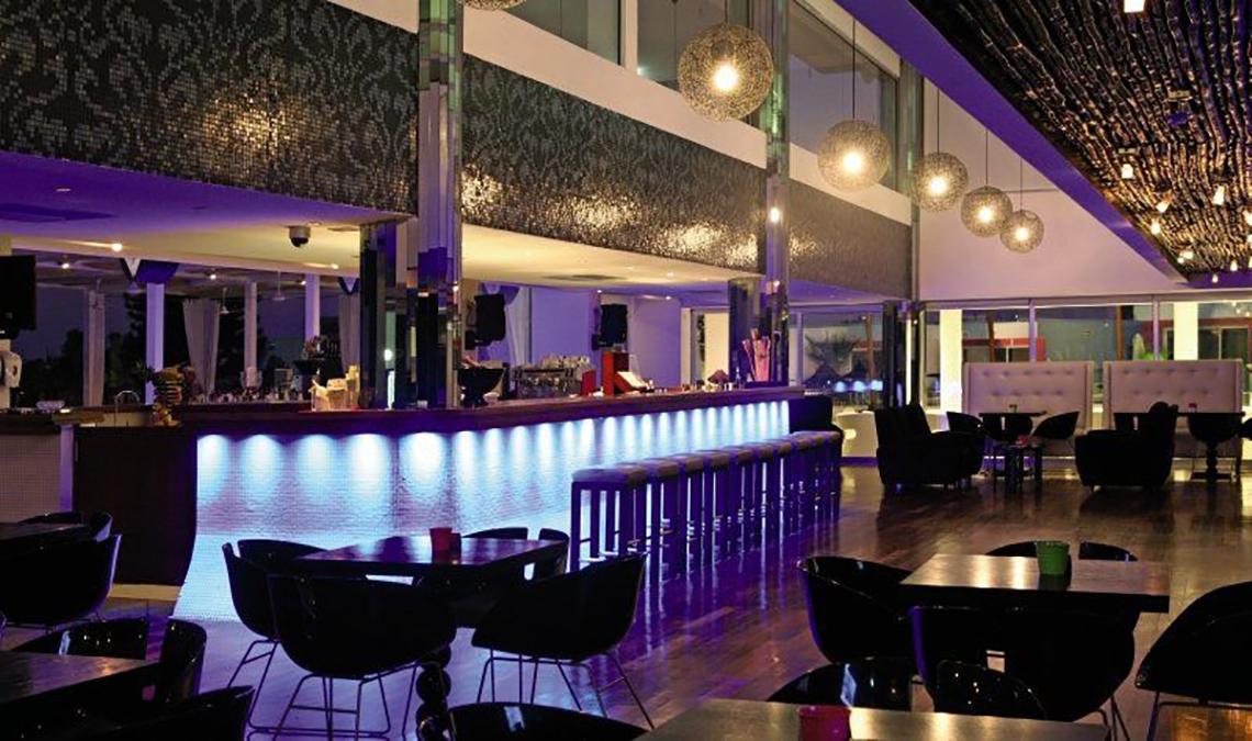 Innenansicht der Bar im Napa Mermaid Hotel & Suites mit lila Beleuchtung, Thekenhockern und runden Tischen.