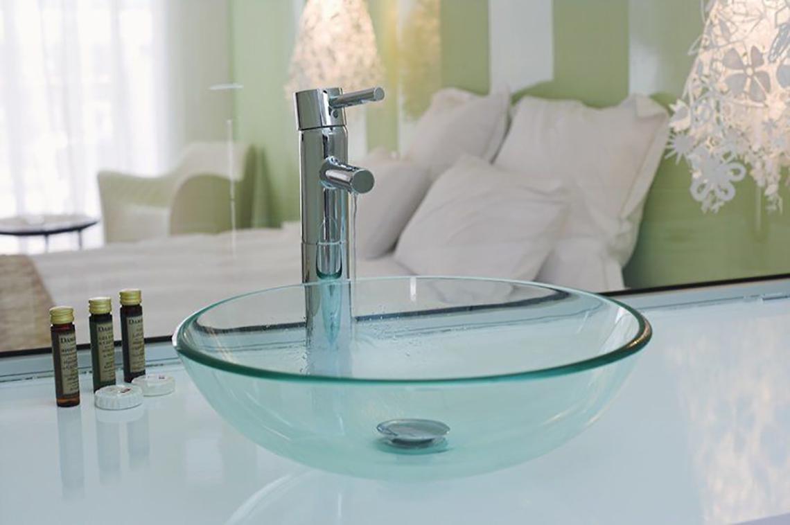 Glasbecken im Badezimmer des Napa Mermaid Hotels mit Chromhahn und grünem Hintergrund.