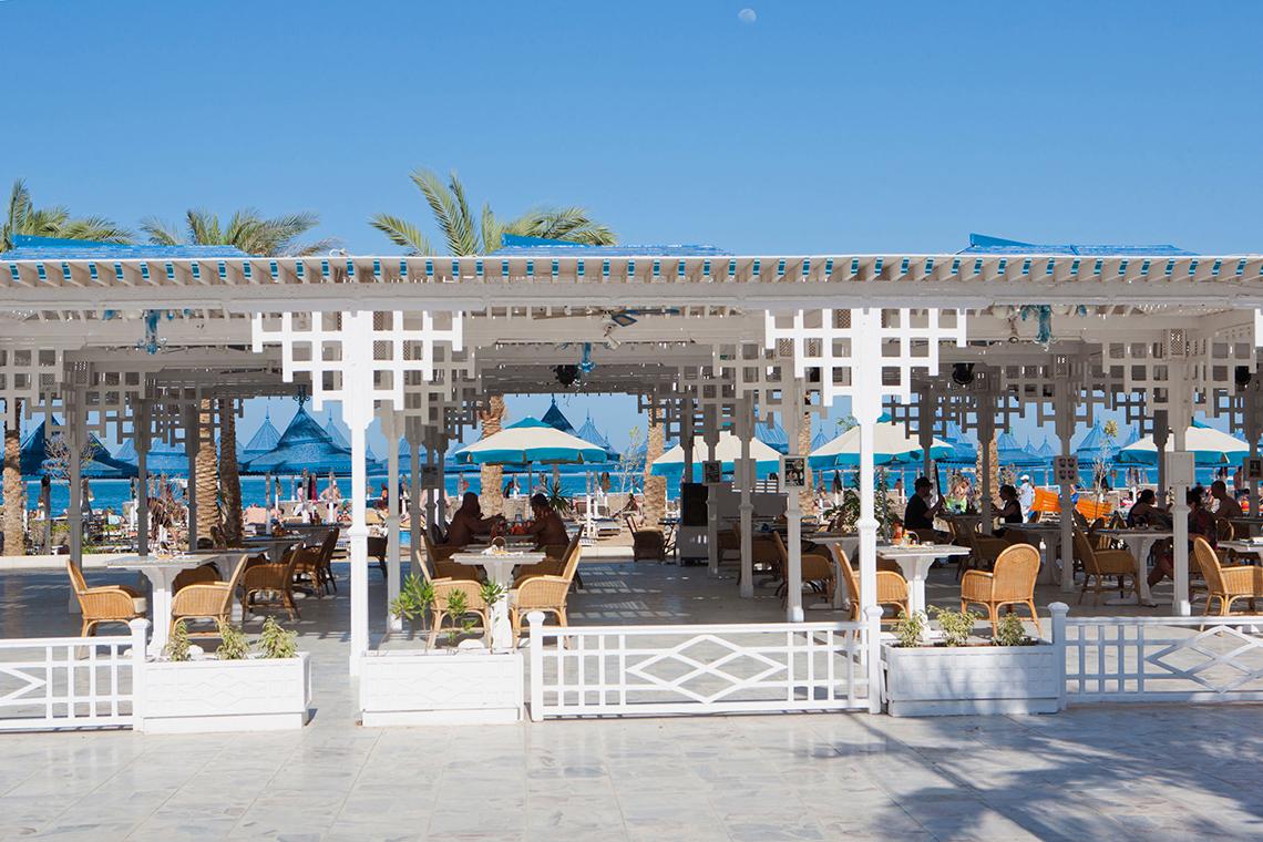 Außenterrasse des Grand Hotel Hurghada mit blauen Sonnenschirmen und Tischen im Freien.