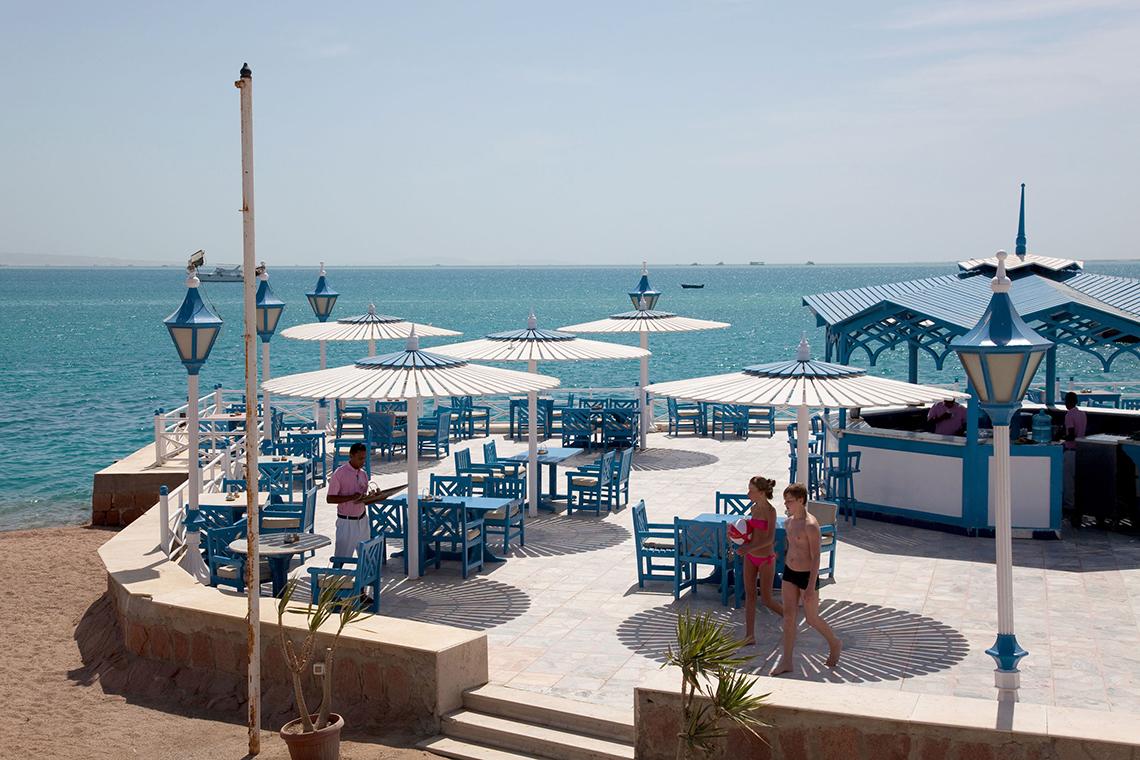 Außenterrasse des Grand Hotel Hurghada mit Blick auf das Meer und mehreren blauen Sonnenschirmen.