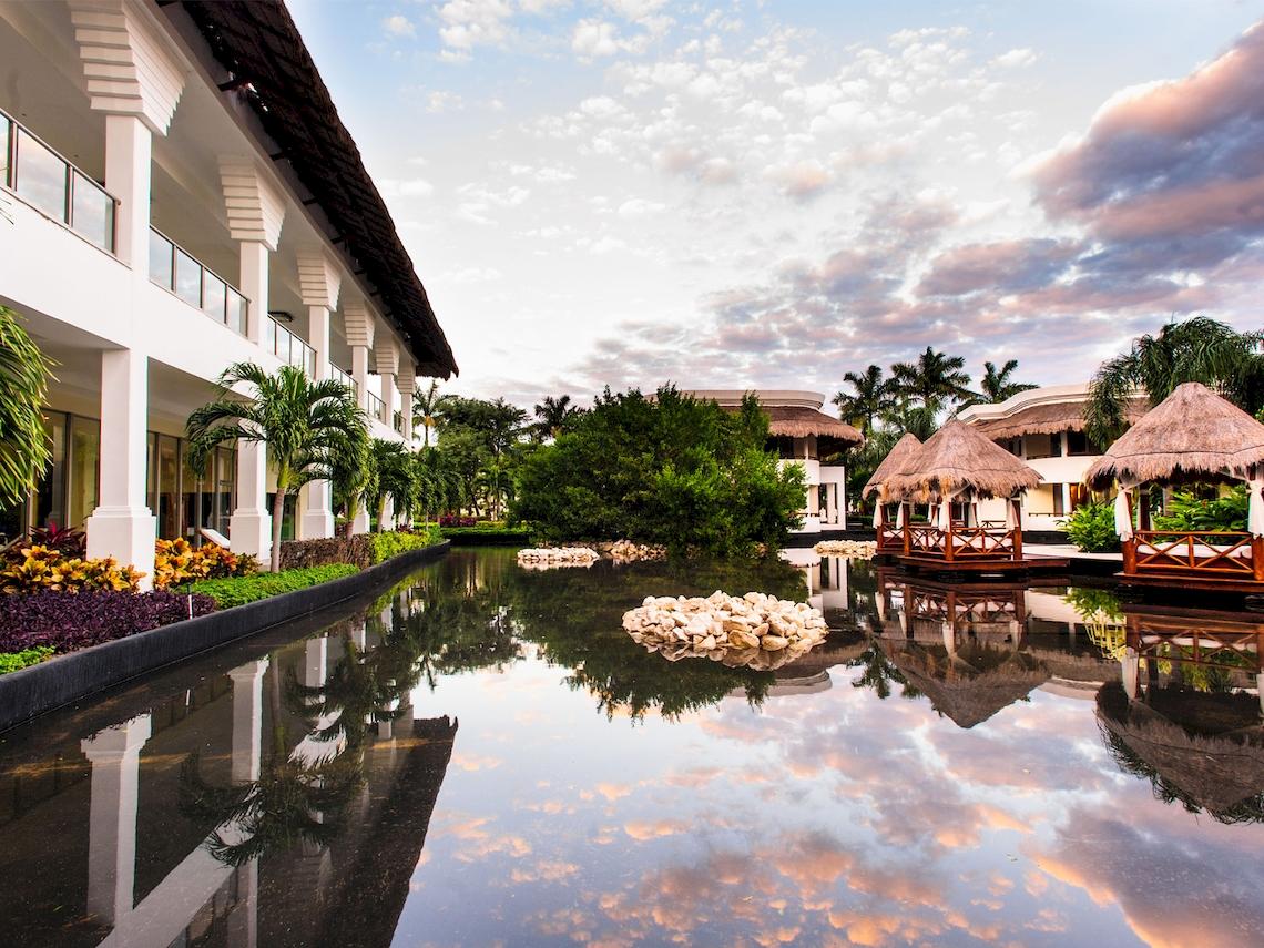 Außenansicht des Grand Sunset Princess All Suites Resort mit Gebäuden, Wassergraben und Pflanzen