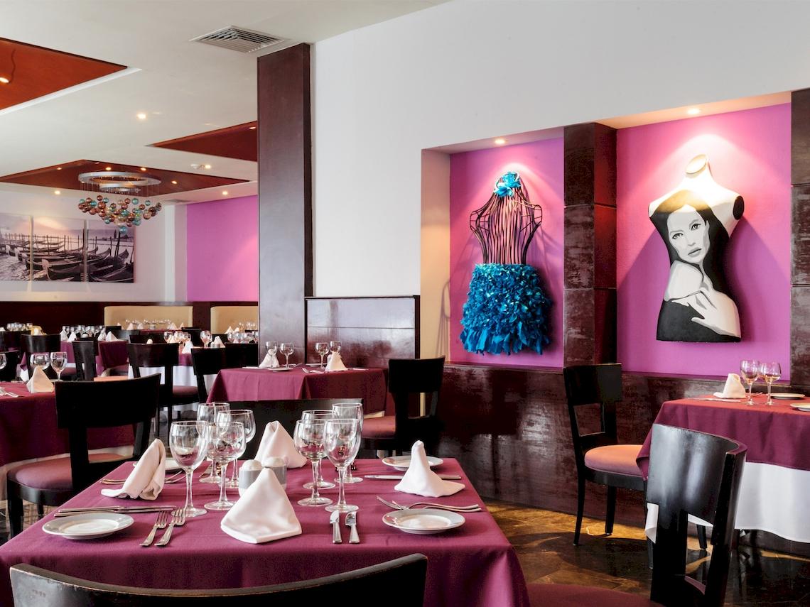 Innenbereich des Restaurants im Grand Sunset Princess All Suites Resort mit Tischdekoration und Kunstwerken an der Wand.
