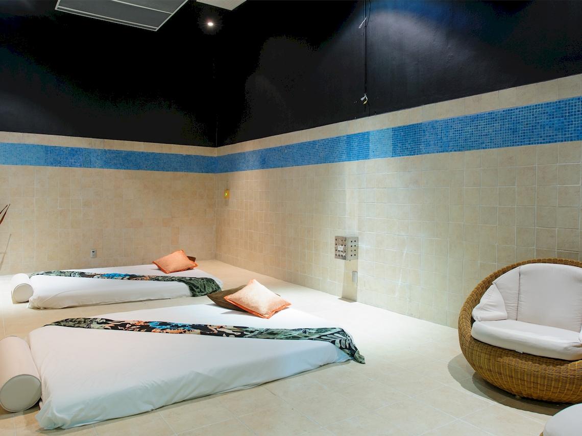 Massageraum im Grand Sunset Princess All Suites Resort mit zwei Betten, Kissen und einer Korbsessel.