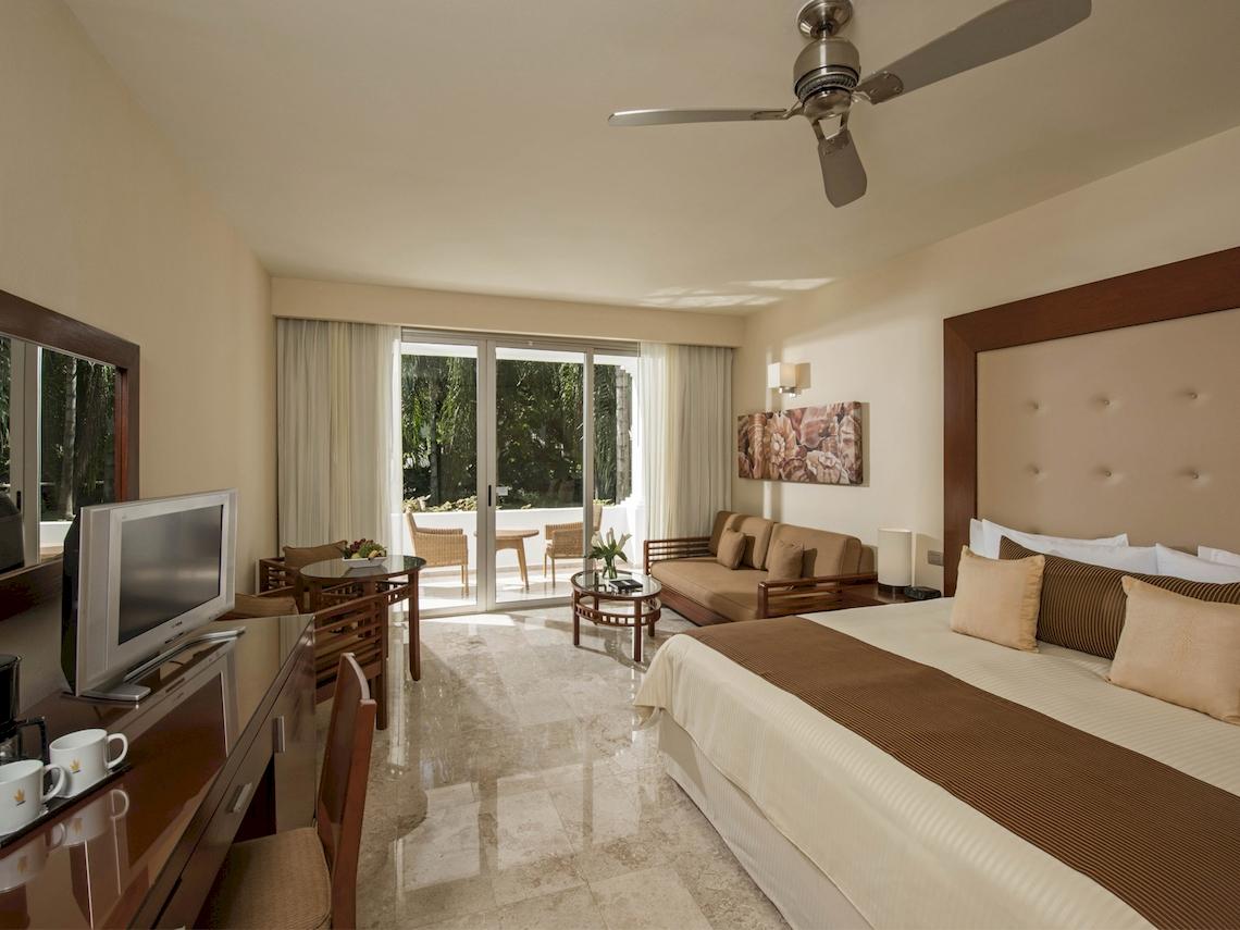 Schlafzimmer im Grand Sunset Princess All Suites Resort mit Bett, Fernseher, Schreibtisch und Terrasse.