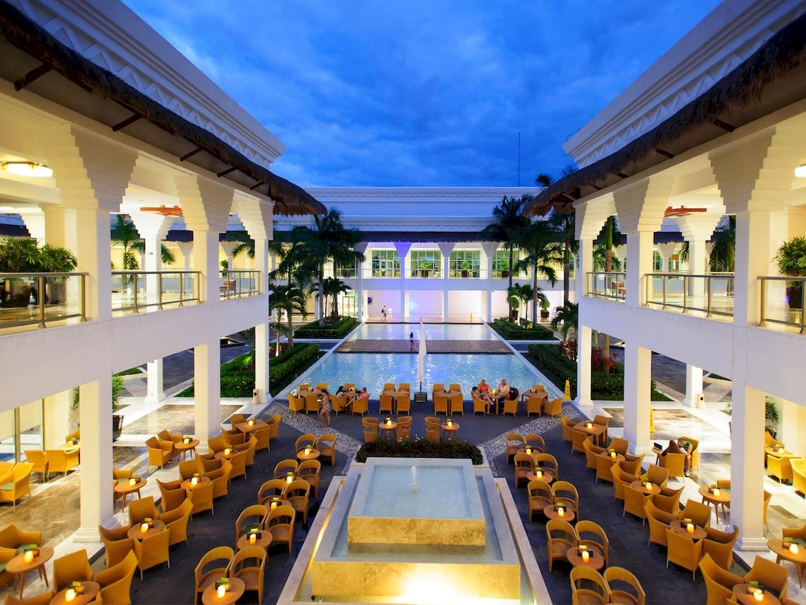 Innenbereich des Grand Sunset Princess All Suites Resorts mit Swimmingpool, Tischen und Stühlen.