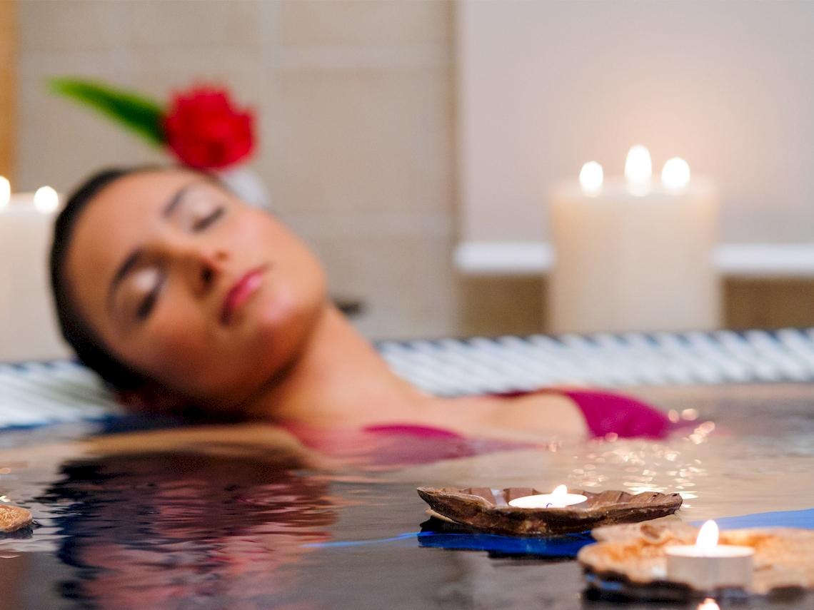 Eine Frau schläft in einer Badewanne mit Kerzen und Blumen.