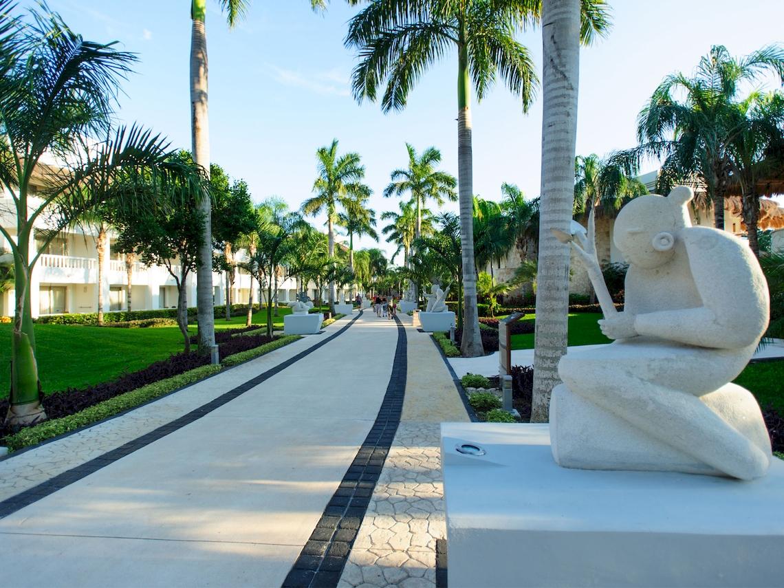 Außenbereich des Grand Sunset Princess All Suites Resorts mit Allee und Palmen.