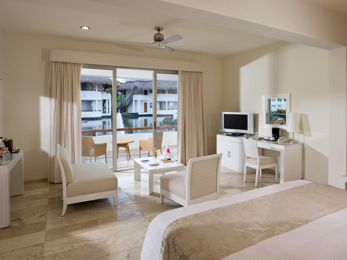 Innenansicht eines modernen Hotelzimmers mit Schlafzimmer, Sitzbereich und Blick auf den Pool.