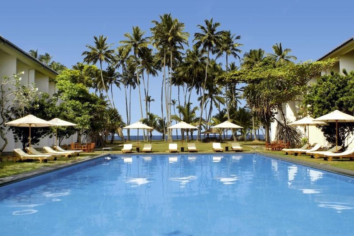 Außenbereich des Mermaid Hotel & Club mit Swimmingpool und Liegestühlen unter Sonnenschirmen.
