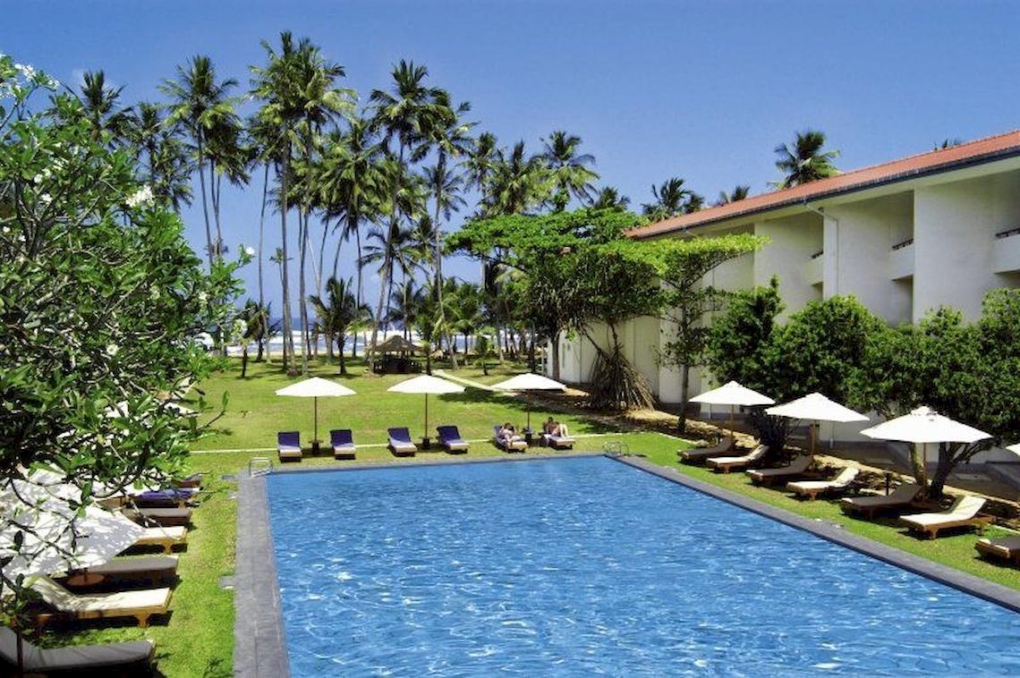 Außenpool und Terrasse des Mermaid Hotel & Club mit Sonnenliegen und Schirmen.